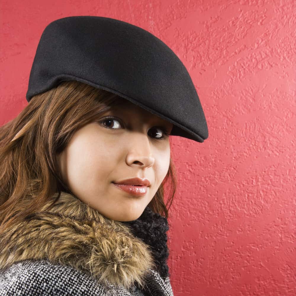 This is a close look at a woman wearing a fur-lined jacket with her black ivy cap.