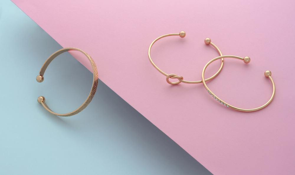 Three gold bangles against blue and pink background.