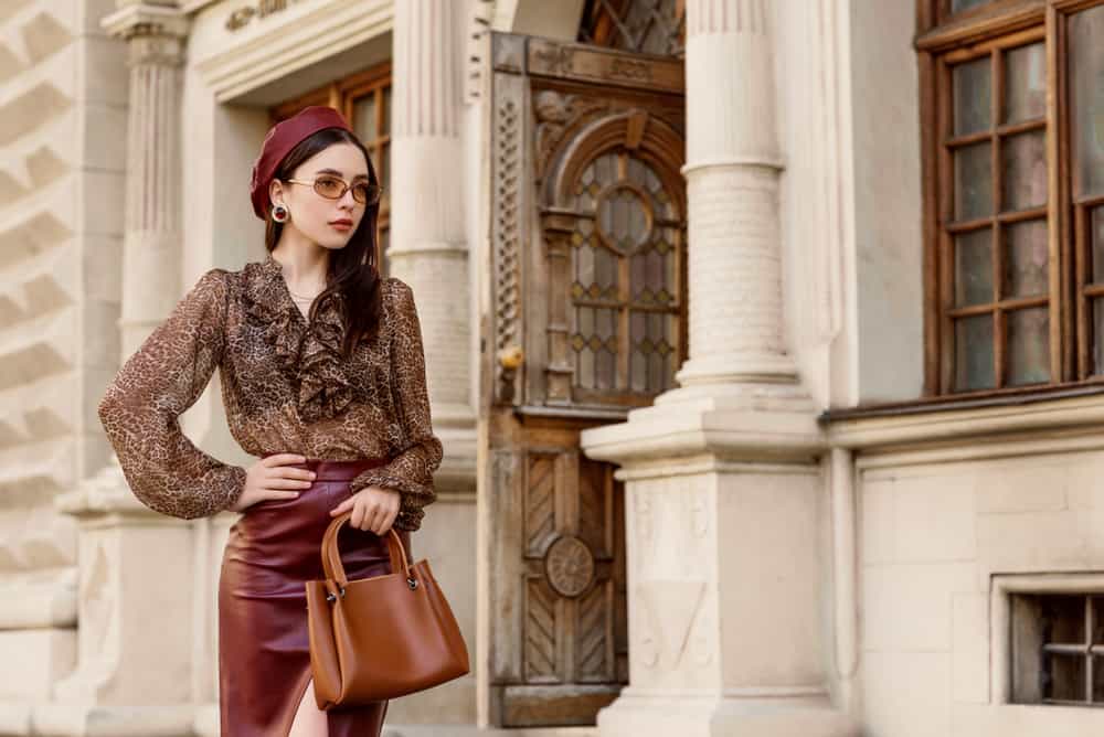 Woman wearing leather beret, skirt, leopard print blouse, beige sunglasses, and a leather handbag.