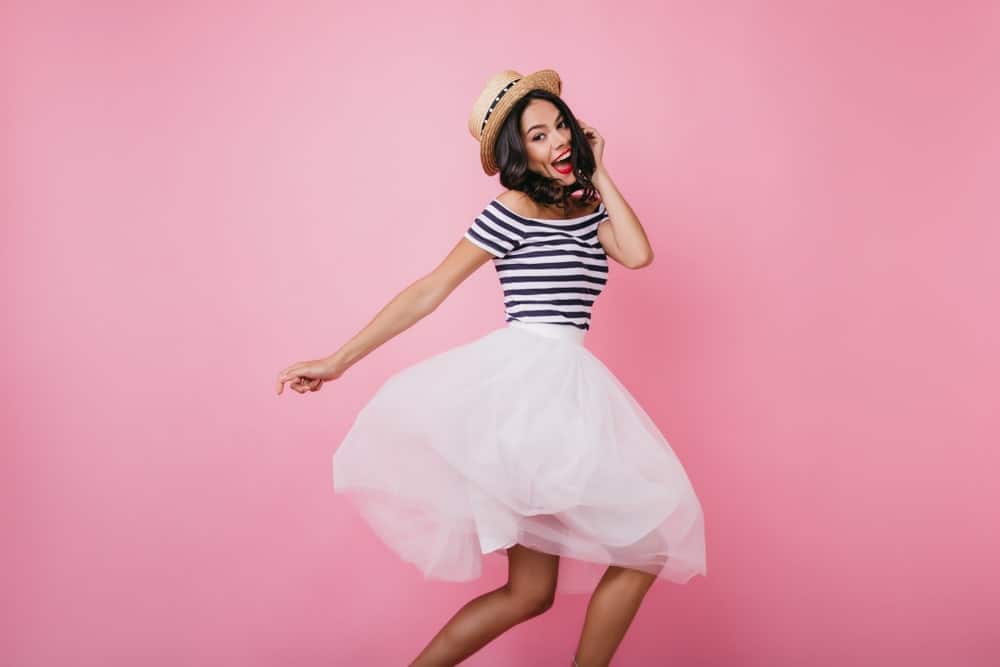 Cheerful woman wearing a straw hat, striped shirt, and white bubble skirt.