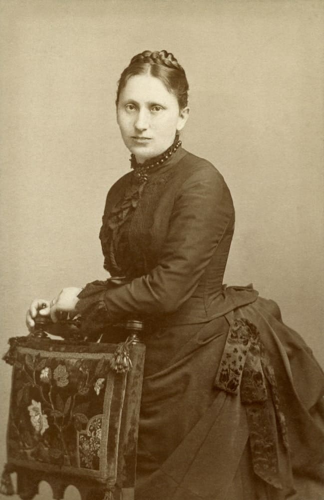 Victorian woman posing behind a chair.