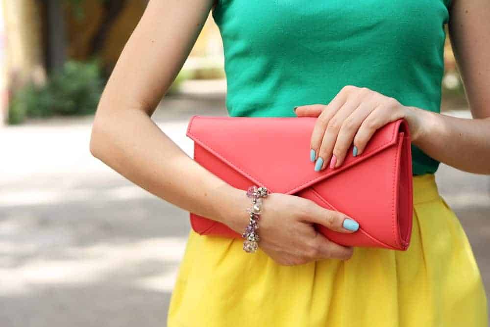 Woman in bright outfit with orange clutch bag.