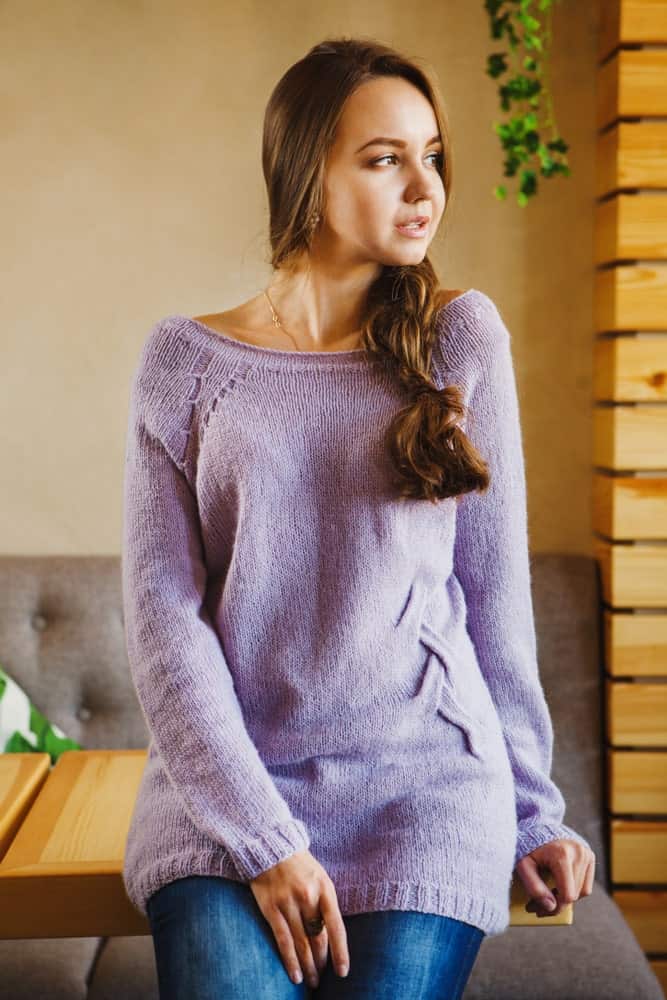 Woman in a purple fanny sweater sitting on a wooden table.