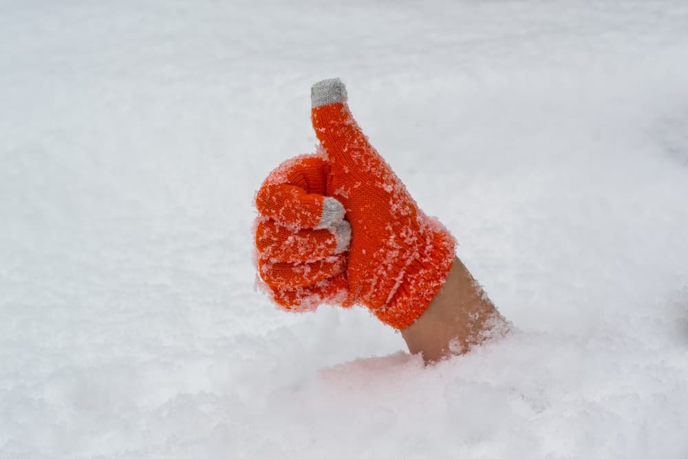 A hand in orange glove thumbs up from under the snow.