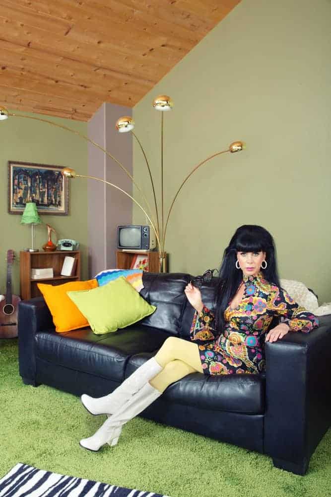 A woman in retro outfit and go-go boots sitting on a black leather sofa.