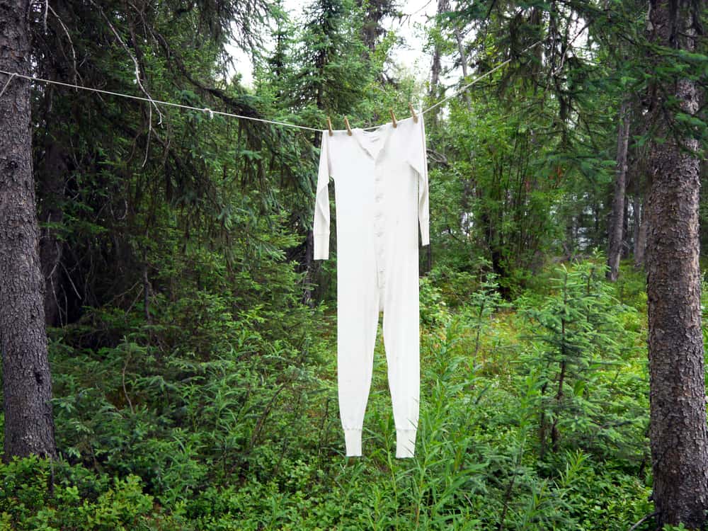 Long underwear hanging on clothesline between forest trees. 