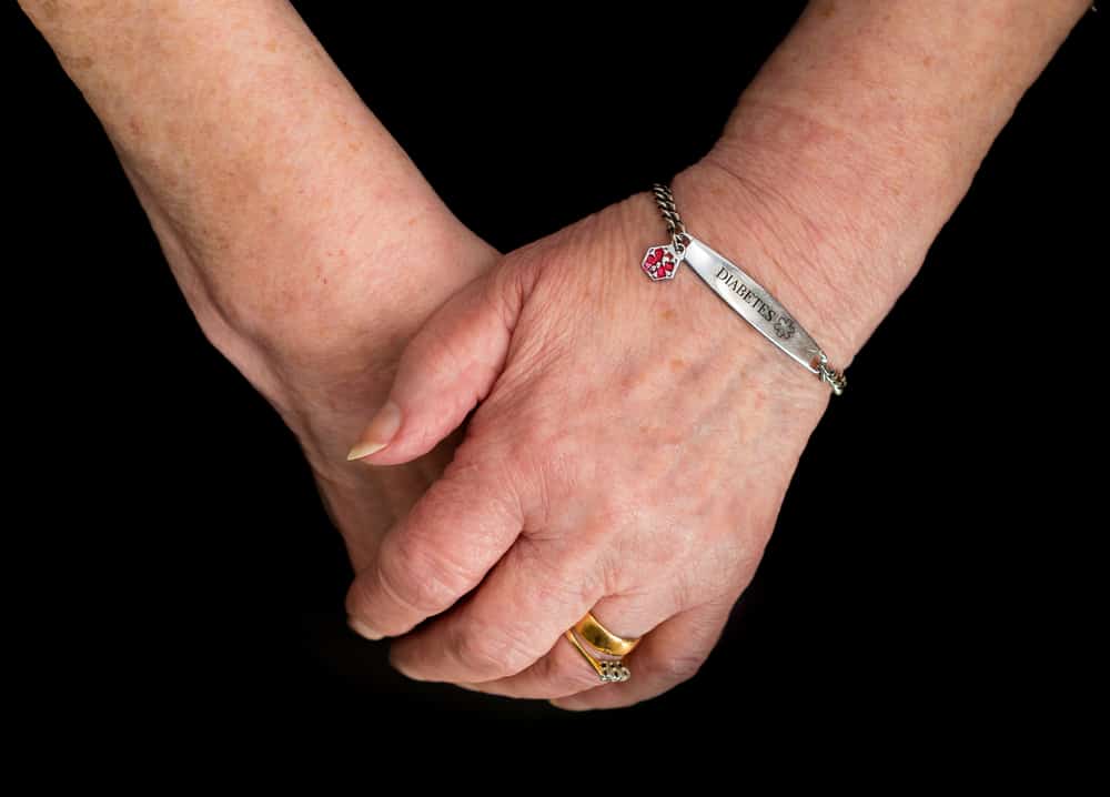 Elderly woman's hands wearing a medical alert bracelet for diabetes.