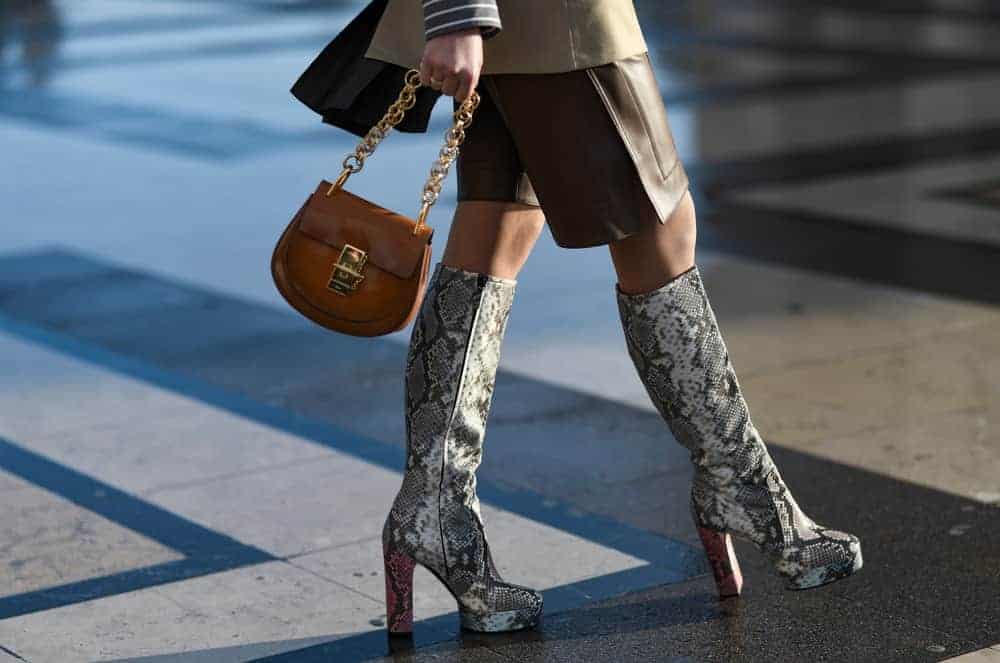A woman walking down the street wearing a snake print platform boots and brown leather chain bag.