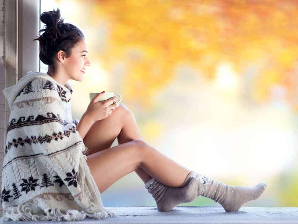 Woman holding a cup of coffee covered in a pancho sweater.