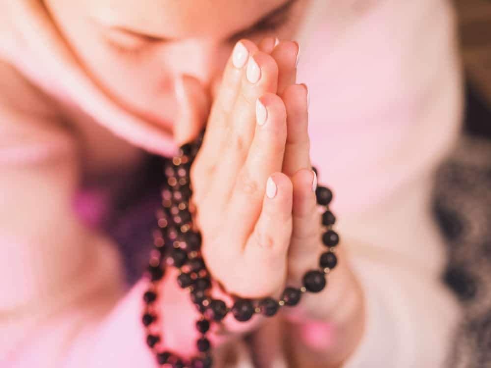 Woman praying while wearing rosary beads.