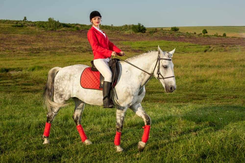 A woman wears a redingote while riding a horse.