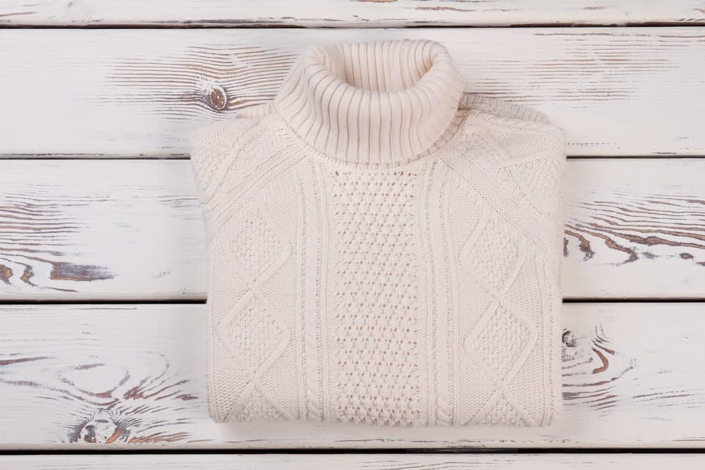  A folded roll-neck sweater against a white wood plank background.
