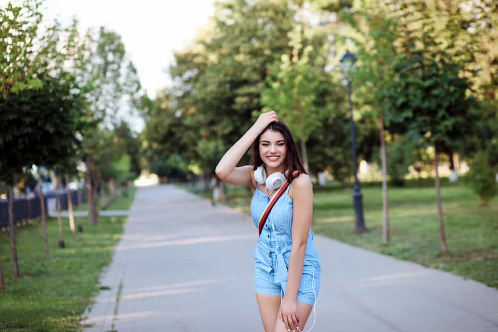 Woman wearing blue rompers and white headphones around her neck at the park.