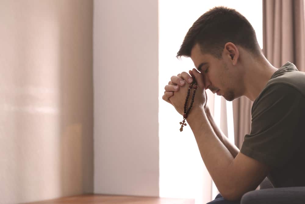 Young man holding rosary beads as he prays at home.