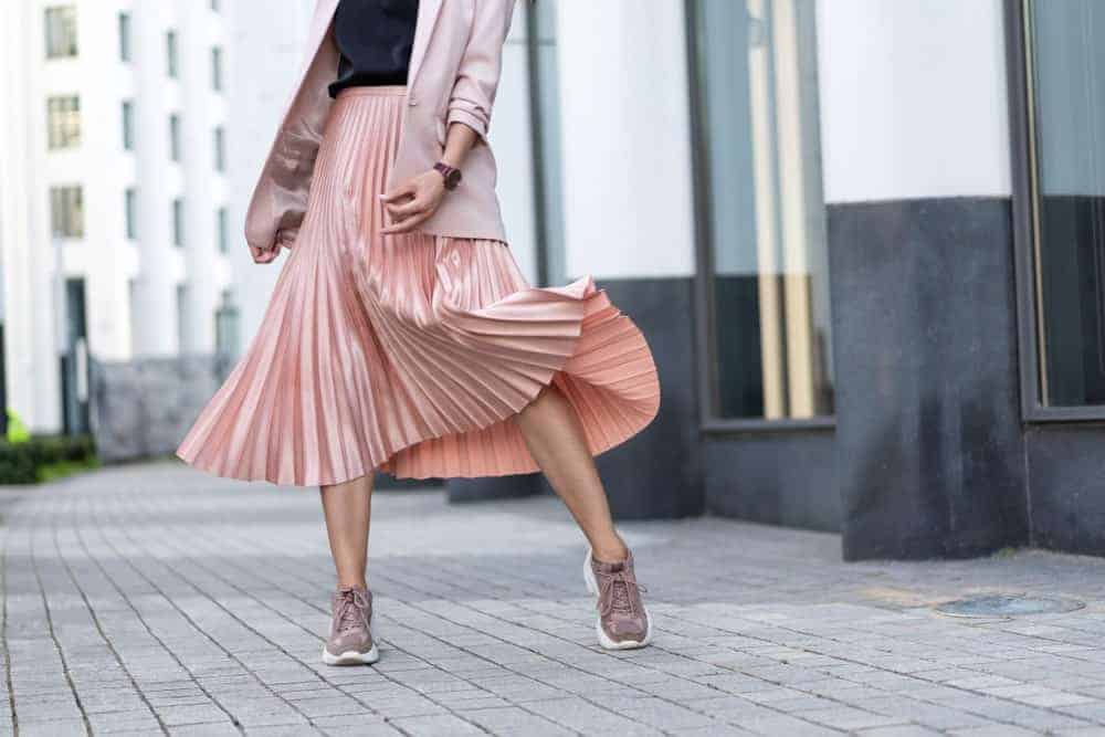 Woman with coral pleated skirt and sneakers.