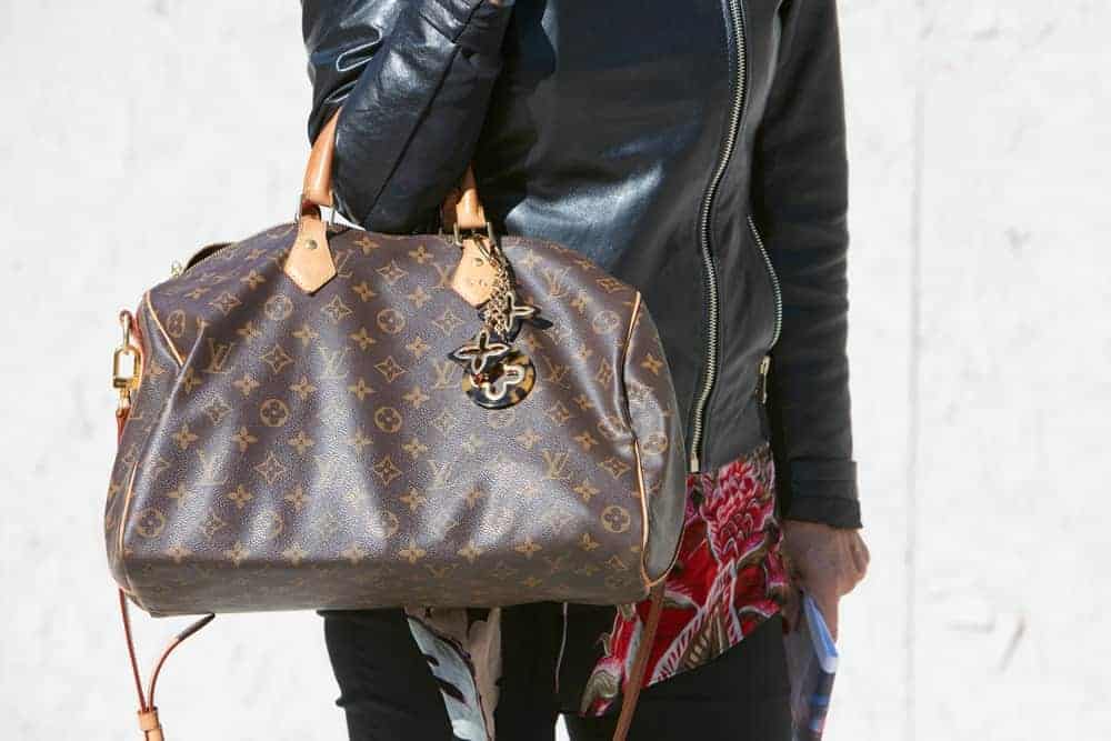 Woman in black leather jacket carrying a Louis Vuitton speedy bag.