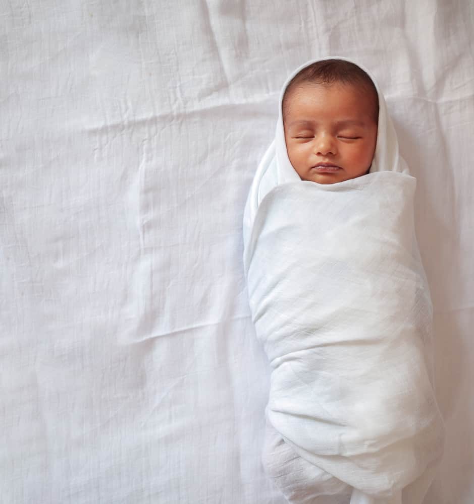 A one month old baby sleeping and swaddled in white cloth.