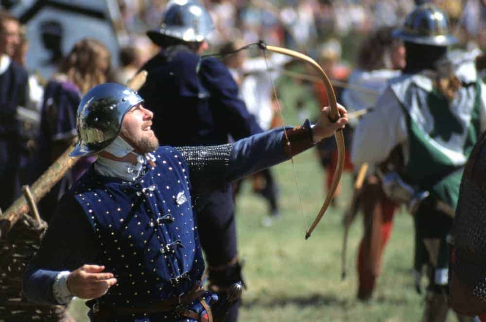 An English Archer fires an arrow from his bow wearing period Medieval helmet and tabard.