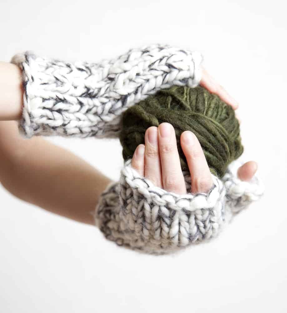 A pair of hands wearing wrist warmers and holding a ball of yarn.