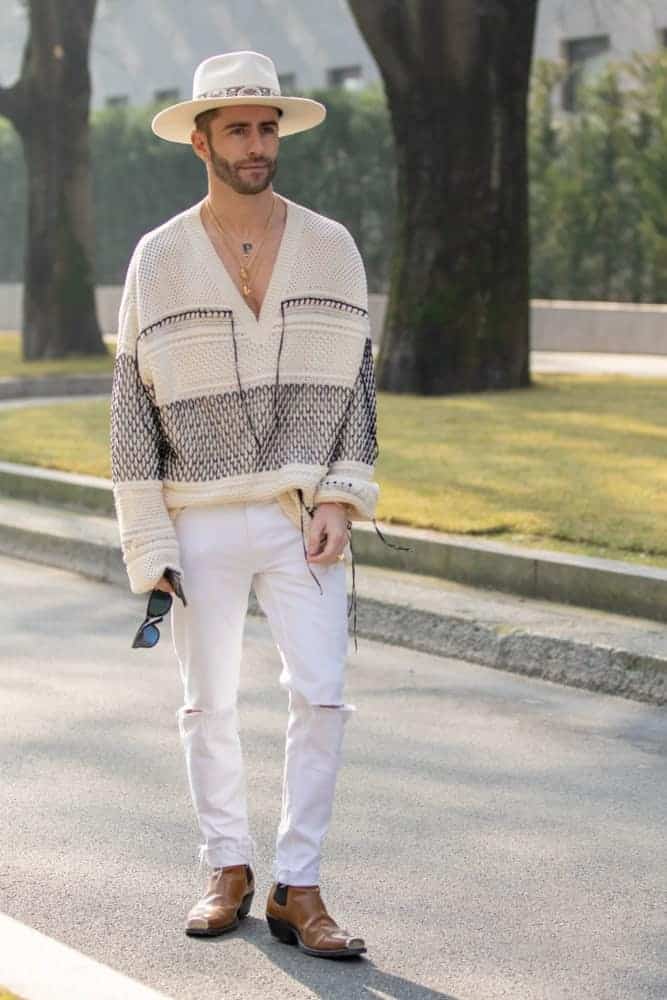 Model wearing a V-neck sweater, white pants, and a Panama hat.