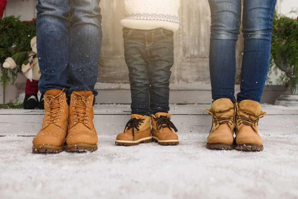 Cropped photo of a family showing their legs with denim pants and winter boots.