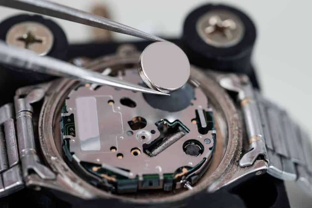 A wristwatch battery being installed with a pair of tweezers.