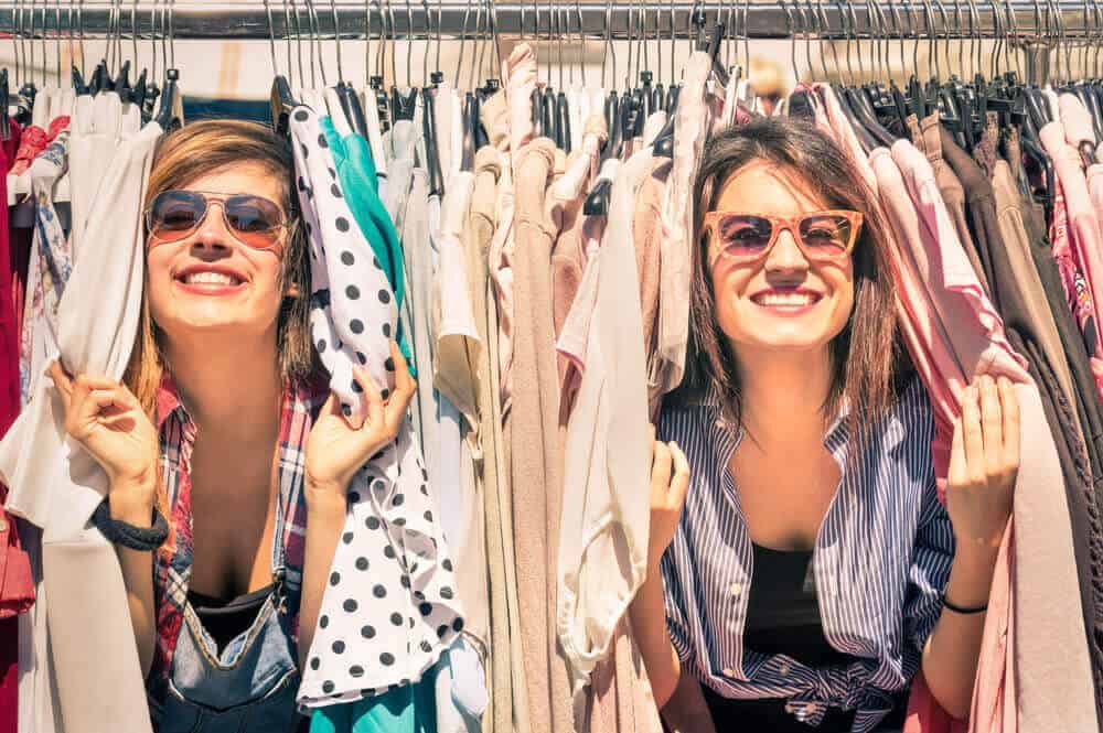 A couple of women having fun at the rack of vintage clothes.