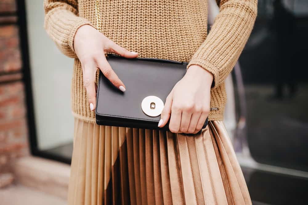 A close look at a woman carrying a black leather clutch bag.