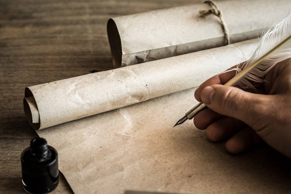 A feather quill pen being used to write on brown paper.