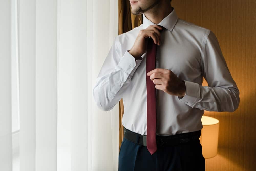 A man wearing a dress shirt without pockets adjusting his necktie.