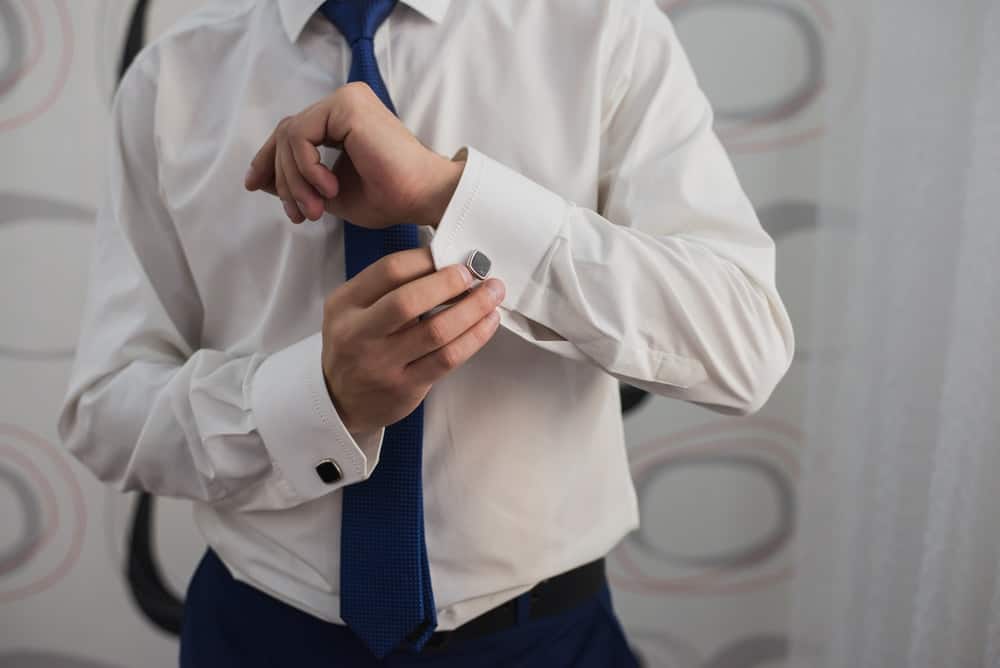 A man putting on cufflinks to his dress shirt without pockets.