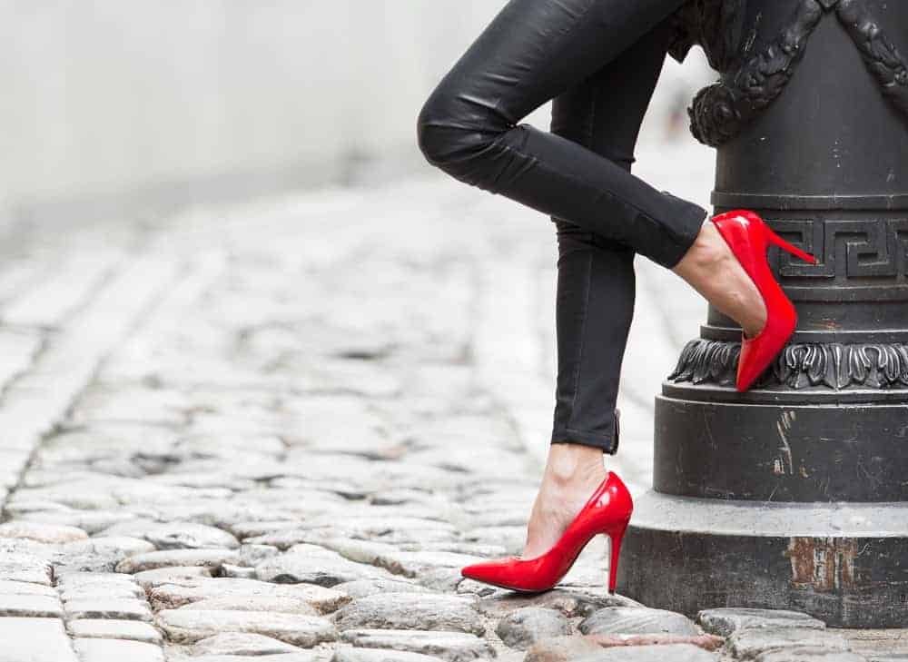 A woman wearing a pair of red high-heeled shoes with her black leather pants.