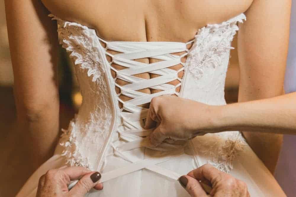 A bride being assisted into her corset.