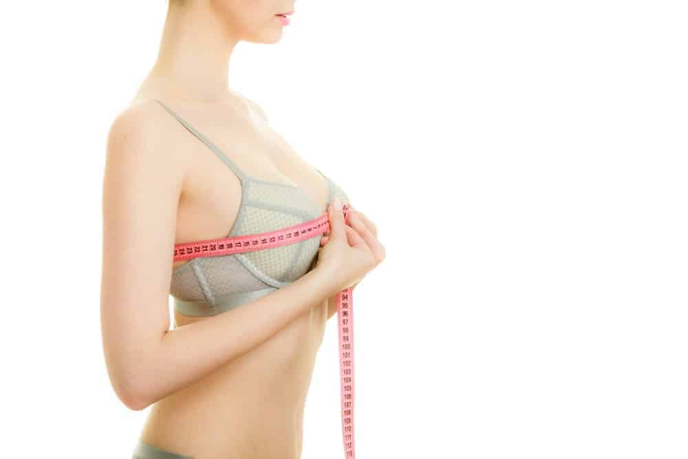 A woman wearing a bra measuring her bust.