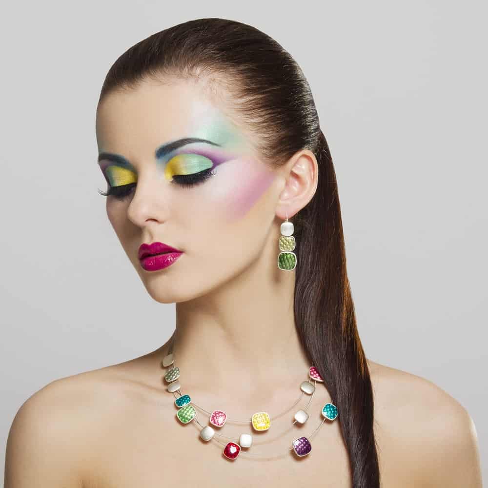 A woman with brightly-colored makeup wearing colorful earrings that match her necklace.