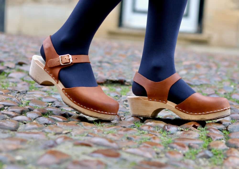 A woman walking on the cobblestones wearing wooden clog shoes with leather straps.