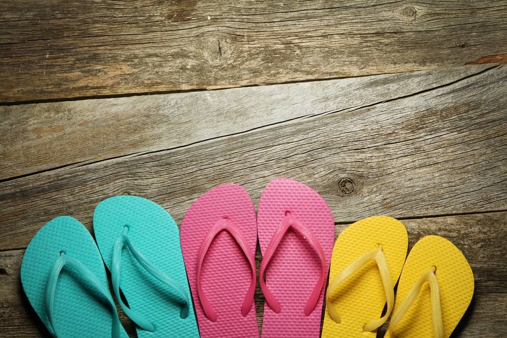 Pairs of colorful flip flops on a wooden floor.