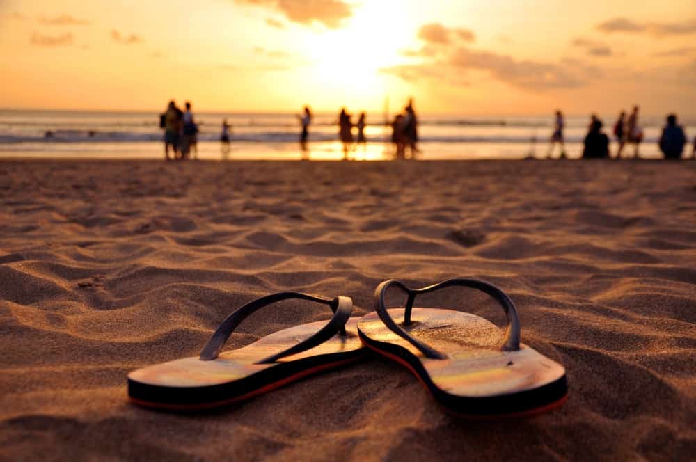 A pair of flip flops on a sandy beach at sunset.