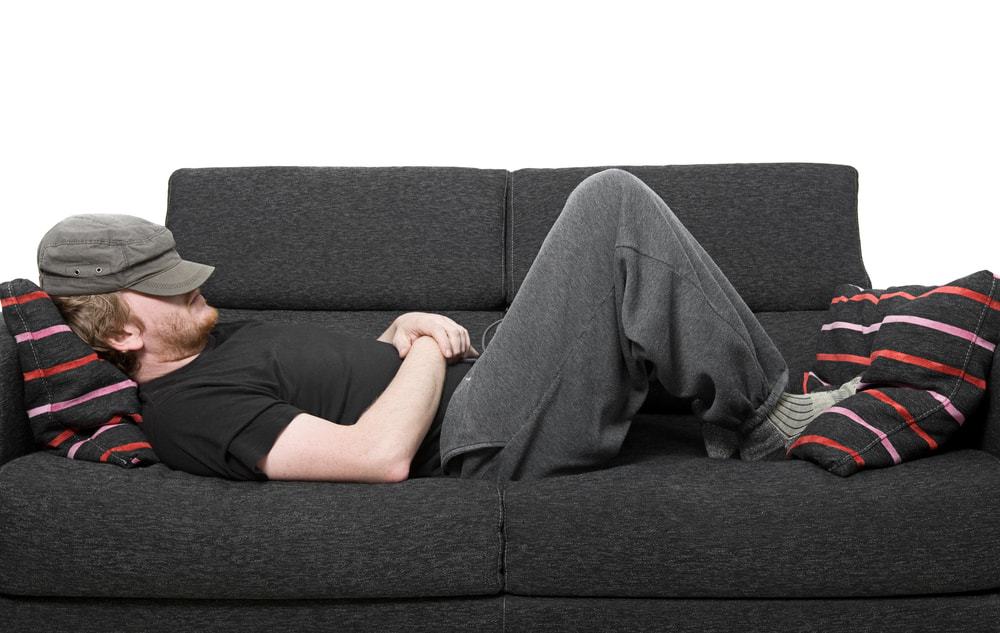 A man wearing sweatpants asleep on the couch.