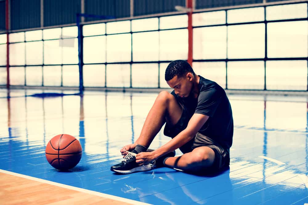 Man tying his shoe laces on a basketball court.