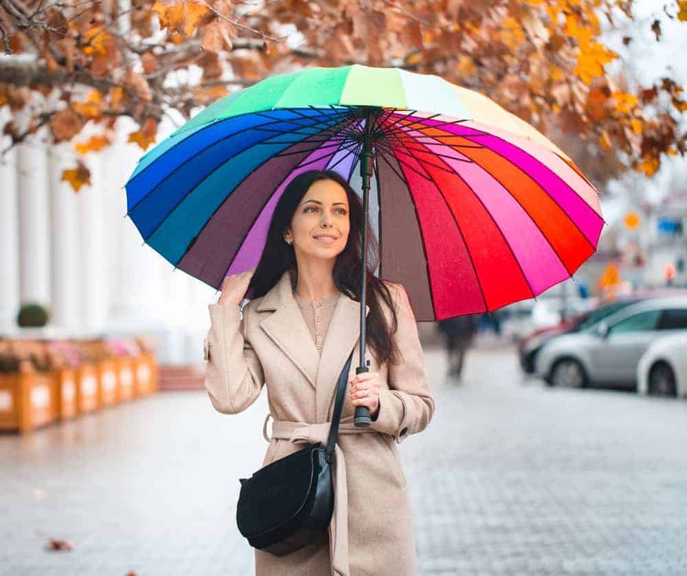 A woman wearing a trench coat with a colorful umbrella.