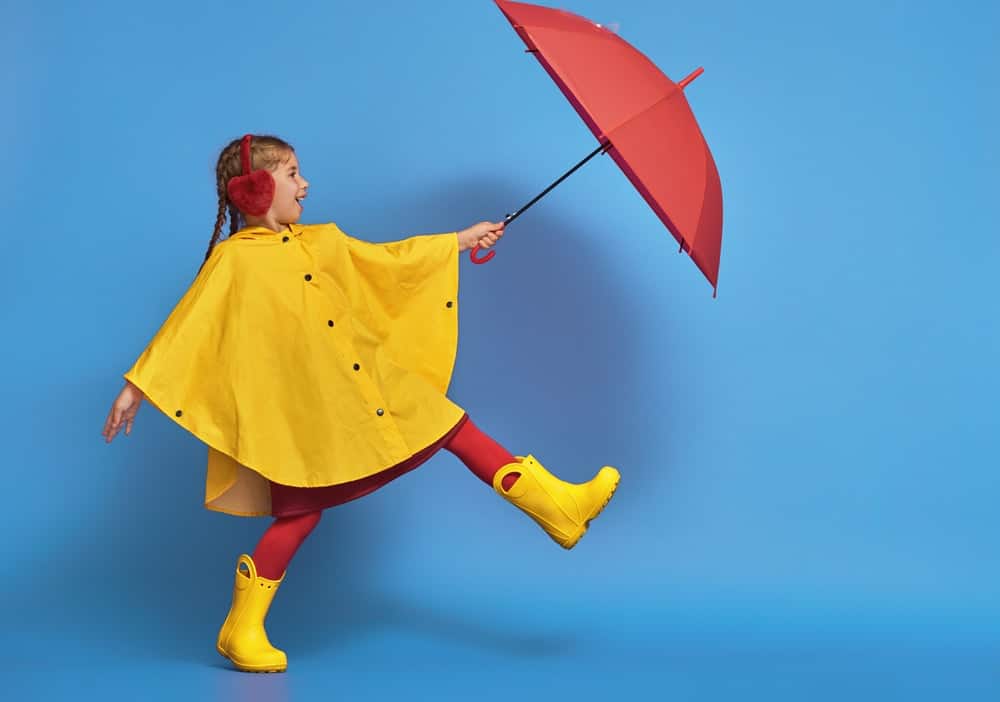 A girl wearing a yellow poncho raincoat that pairs with her boots.