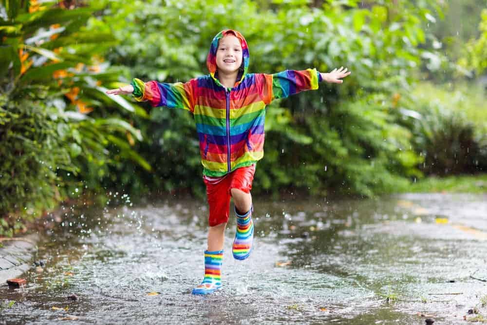 A boy wearing a rainbow jacket and boots.