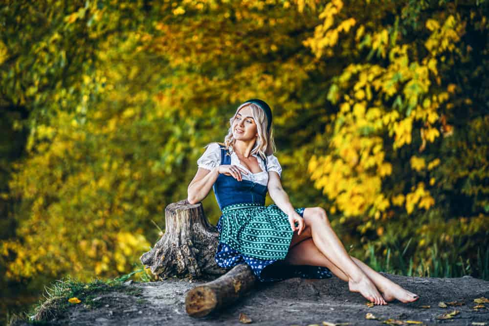 Woman in a green dirndl dress sitting outudoors.