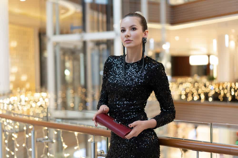 Woman in a shopping center wearing black sequin dress and a red clutch.