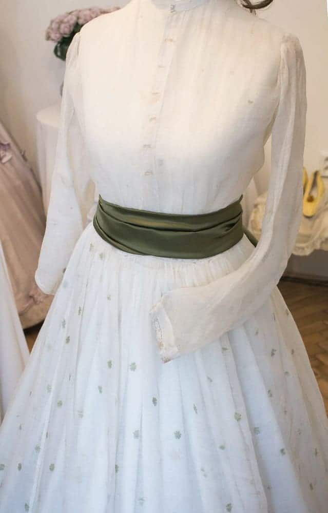 A close look at a white dress with a green sash belt on display.
