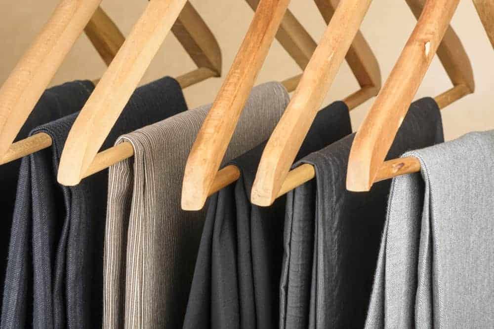 Multiple pairs of pants supported by wooden pant hangers.