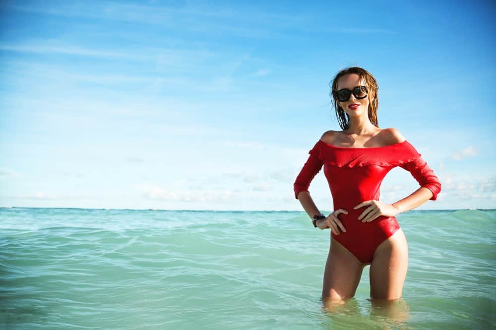A woman posing at the beach wearing a red swim dress.