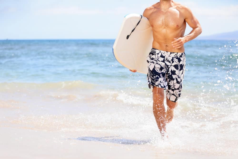 A surfer wearing floral board shorts at the beach.