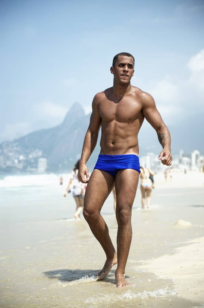 A man wearing blue swim briefs at the beach.